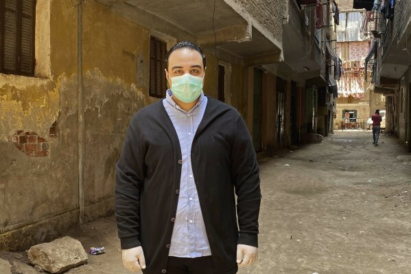 In this April 17, 2020 photo, Dr. Sherif Waheed poses on a street where 73-year-old Ghaliya Abdel-Wahab died from COVID-19 on April 6, 2020, on one of two streets on complete lockdown closed off by security forces for people to quarantine after her death, in Bahtim, Shubra el-Kheima neighborhood, Qalyoubiya governorate, Egypt. (AP Photo/Nariman El-Mofty)