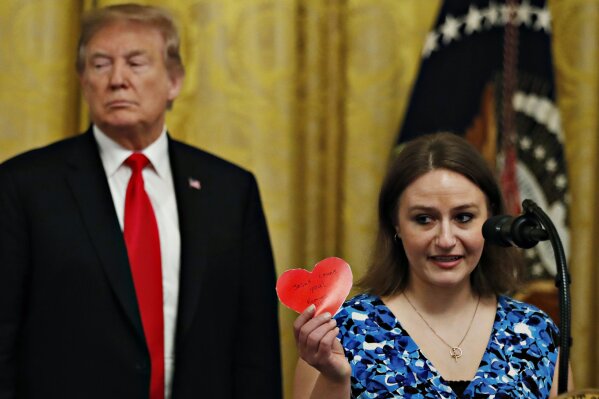 
              Polly Olson holds up a heart that says "Jesus Loves You" during an event with President Donald Trump to sign an executive order requiring colleges to certify that their policies support free speech as a condition of receiving federal research grants, Thursday March 21, 2019, in the East Room of the White House in Washington. Olson said that while attending Northeast Wisconsin Technical College the college had limited her from handing out Valentine's Day cards with religious messaging on campus. (AP Photo/Jacquelyn Martin)
            