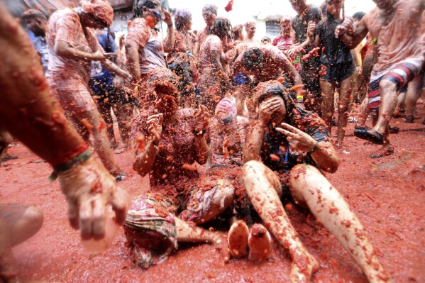 Revellers throw tomatoes at each other during the annual "Tomatina" tomato fight fiesta, in the village of Bunol near Valencia, Spain, Wednesday, Aug. 30, 2023. Thousands gather in this eastern Spanish town for the annual street tomato battle that leaves the streets and participants drenched in red pulp from 120,000 kilos of tomatoes. (AP Photo/Alberto Saiz)