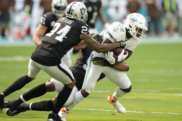 Las Vegas Raiders cornerback Marcus Peters (24) and defensive end Tyree Wilson tackle Miami Dolphins running back De'Von Achane (28) during the first half of an NFL football game, Sunday, Nov. 19, 2023, in Miami Gardens, Fla. (AP Photo/Wilfredo Lee)