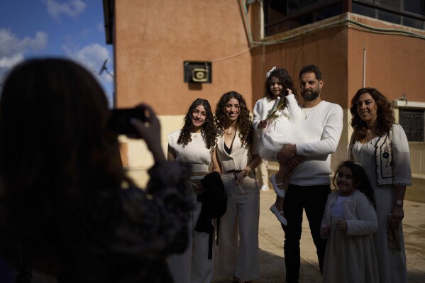 A Christian Lebanese family poses for a photo during Palm Sunday Mass at the Maronite Church of St. George in Quraye, near the southern port city of Sidon, Lebanon, Sunday, April 13, 2025. (AP Photo/Hassan Ammar)