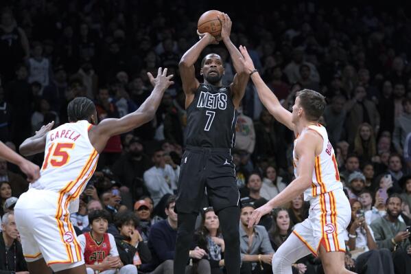 Brooklyn Nets forward Kevin Durant (7) shoots a 3-point basket past Atlanta Hawks center Clint Capela (15) and guard Bogdan Bogdanovic (13) during the second half of an NBA basketball game Friday, Dec. 9, 2022, in New York. The Nets won 120-116. (AP Photo/Mary Altaffer)