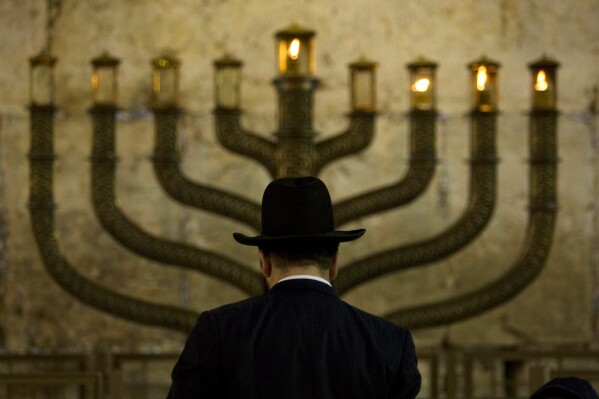 FILE - An Ultra-Orthodox Jewish man stands in front of a menorah on the third eve of Hanukkah, at the Western Wall, Judaism's holiest site in Jerusalem's old city, Sunday, Dec. 13, 2009. On eight consecutive nightfalls, Jews gather with family and friends to light one additional candle in the menorah candelabra. They do so to commemorate the rededication of the Temple in Jerusalem in the 2nd century BC, after a small group of Jewish fighters liberated it from occupying foreign forces. (APPhoto/Sebastian Scheiner, File)
