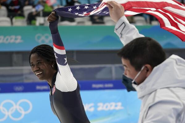 FILE - Erin Jackson holds up a U..S. flag with coach Ryan Shimabukuro after winning the gold medal in the women's 500-meter speedskating race at the Winter Olympics, Sunday, Feb. 13, 2022, in Beijing. Fresh off the best Olympic showing by the U.S. speedskating team in a dozen years, Shimabukuro is staying on for another four years as coach of the American squad. Shimabukuro posted a picture on his Facebook page Tuesday showing him signing his new contract at the Utah Olympic Oval in suburban Salt Lake City.  (AP Photo/Ashley Landis, File)
