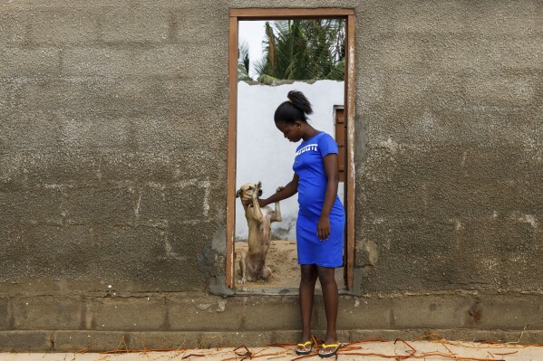 Afeli Bernice Adzo plays with her dog named Nuworza at the entrance of her room, which was destroyed by coastal erosion in Avegadzi, Ghana, Wednesday, March 5, 2025 (AP Photo/Misper Apawu)