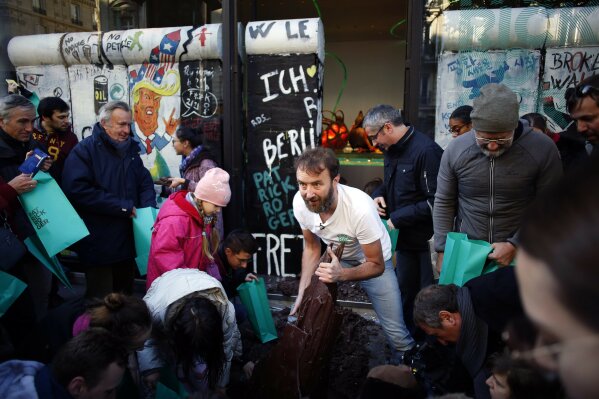 French chocolate maker Patrick Roger, center, destroys a reproduction of the Berlin wall in chocolate, to mark the 30th anniversary of the fall of the Berlin Wall, in Paris, Saturday, Nov. 9, 2019. (AP Photo/Thibault Camus)