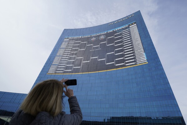 FILE - Lisa Moeller takes a photo of the NCAA bracket for the NCAA college basketball tournament on the side of the JW Marriott in downtown Indianapolis, March 17, 2021. (AP Photo/Darron Cummings, File)