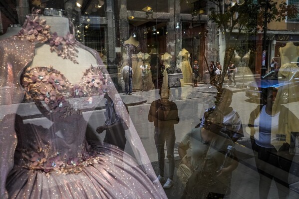 Pedestrians browse bridal dresses in a storefront window, Thursday, May 30, 2024, in Mexico City. Mexicans will vote Sunday in an election that prioritizes gender, democracy and populism, deciding the country's future in a vote overshadowed by cartel violence. With two women leading the way, Mexico is likely to elect its first female president. (AP Photo/Matthias Delacroix)