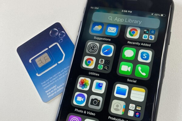 A SIM card is shown next to a cellphone in this photo taken on Tuesday, June 11, 2024 in London. Physical SIM cards are going away, replaced by eSIMs which make switching cell carriers easier. AP Photo/Kelvin Chan)