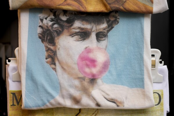 A souvenir bag showing Michelangelo's 16th century statue of David blowing a bubble gum on sale among other souvenirs in a shop in downtown Florence, central Italy, Monday, March 18, 2024. Michelangelo’s David has been a towering figure in Italian culture since its completion in 1504. But curators worry the marble statue’s religious and political significance is being diminished by the thousands of refrigerator magnets and other souvenirs focusing on David’s genitalia. The Galleria dell’Accademia’s director has positioned herself as David’s defender and takes swift aim at those profiteering from his image. (AP Photo/Andrew Medichini)