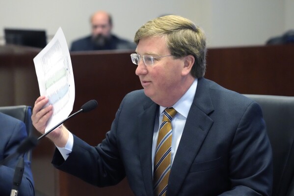 Mississippi Gov. Tate Reeves waves a sheet of revenue projections as he refuses to approve top lawmakers' proposed revenue estimates Wednesday, Nov. 15, 2023, during a meeting of the Joint Legislative Budget Committee, in Jackson, Miss. Reeves believes a lower projection than he wanted would make it more difficult to justify future income tax cuts. (AP Photo/Rogelio V. Solis)