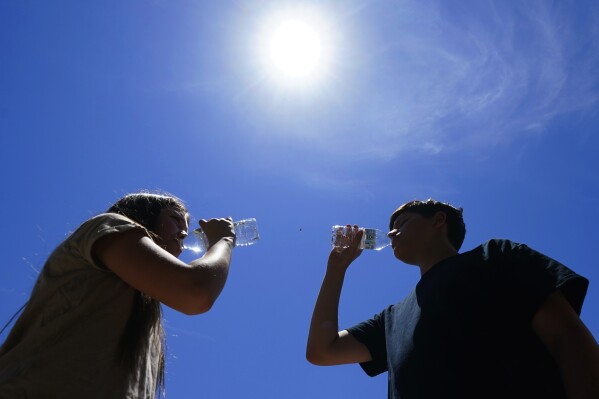 FILE - Tony Berastegui Jr., right, and his sister Giselle Berastegui drink water, Monday, July 17, 2023, in Phoenix. A historic heat wave that turned the Southwest into a blast furnace throughout July is beginning to abate with the late arrival of the monsoon rains. Forecasters expect that by Monday, July 31, at the latest, people in metro Phoenix will begin seeing high temperatures under 110 degrees Fahrenheit (43.3 degrees Celsius) for the first time in a month. (AP Photo/Ross D. Franklin, File)