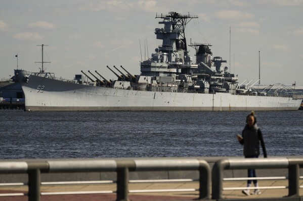 A person walks in Philadelphia across the Delaware River from the USS New Jersey in Camden, N.J., Tuesday, March 19, 2024. The battleship is scheduled to move from its dock in Camden on March 21, when it will head to the Philadelphia Navy Yard for extensive maintenance work. The USS New Jersey is scheduled to move from its dock in Camden on Thursday, March 21, 2024, when it will head to the Philadelphia Navy Yard for extensive maintenance work. (AP Photo/Matt Rourke)