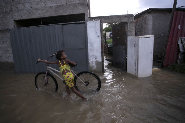A child pushes a bicycle in a flooded street after deadly, heavy rainfall in Duque de Caxias, Brazil, Sunday, Jan. 14, 2024. (AP Photo/Bruna Prado)
