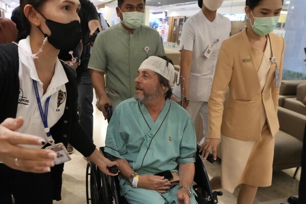 An Australian passenger, center, who was injured on a flight that was battered by severe turbulence, talks to reporters at Samitivej Srinakarin Hospital in Bangkok, Thailand, Thursday, May 23, 2024. The airline's Flight SQ321 was flying from London’s Heathrow airport to Singapore when it hit the turbulence Tuesday, bashing people around inside the plane. (AP Photo/Sakchai Lalit)