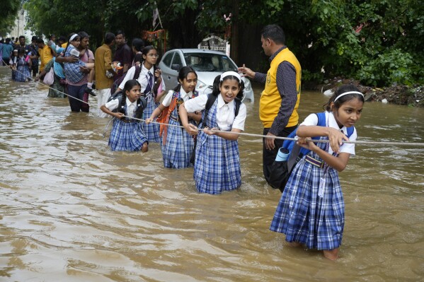 Students hold on to a rope as they cross a street flooded after heavy rains, on their way home in Ajmer, India, Sept. 6, 2024. (AP Photo/Deepak Sharma)