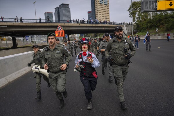 An Israeli activist dressed as a clown runs with border police as Israelis protest against plans by Prime Minister Benjamin Netanyahu's government to overhaul the judicial system block a free way in Tel Aviv, Israel, Thursday, March 23, 2023. (AP Photo/Oded Balilty)