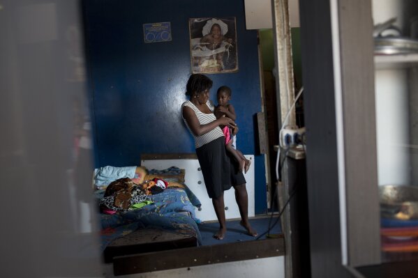 
              In this Oct. 20, 2017, Vanessa holds her son Gabriel inside their home in the Jardim Gramacho slum of Rio de Janeiro, Brazil. For many who live in Rio's hundreds of slums, like Vanessa who makes detergent to sell, an already hardscrabble existence feels increasingly precarious. (AP Photo/Silvia Izquierdo)
            