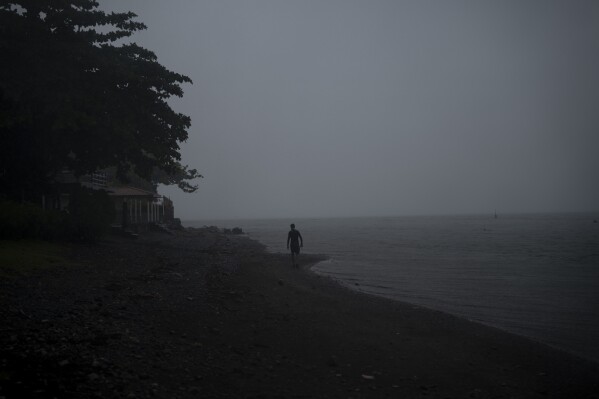 A man walks on a beach during a rainstorm in Te Aupoo, Tahiti, French Polynesia, Monday, Jan. 15, 2024. (AP Photo/Daniel Cole)