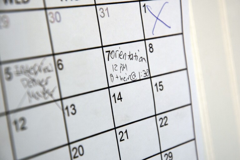 A calendar marking an orientation date hangs on the wall of Eric Martinez's room at a micro community in Denver on Wednesday, June 5, 2024. Martinez along with the others were directed into the micro communities of small cabin-like structures with a twin bed, desk and closet, after his Denver tent encampment was swept. The city built three such communities with nearly 160 units total in about six months, at roughly $25,000 per unit. (AP Photo/Thomas Peipert)