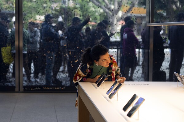 File - As shoppers wait in the background, a woman looks at Apple's new iPhone 15 at an Apple Store in Los Angeles, Friday, Sept. 22, 2023. On Friday, the Commerce Department issues its August report on consumer spending. (AP Photo/Jae C. Hong, File)