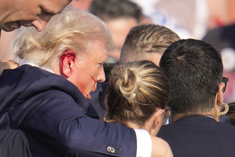 Republican presidential candidate former President Donald Trump is surrounded by U.S. Secret Service agents as he is helped off the stage at a campaign rally in Butler, Pa., Saturday, July 13, 2024. (AP Photo/Gene J. Puskar)