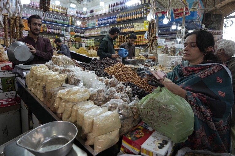A woman pays cash to a shopkeeper after buying grocery items at bazaar in Karachi, Pakistan, Tuesday, Feb. 6, 2024. More than 120 million voters in Pakistan get to elect a new parliament on Thursday. The elections are the twelfth in the country's 76-year history, which has been marred by economic crises, military takeovers and martial law, militancy, political upheavals and wars with India. (AP Photo/Fareed Khan)