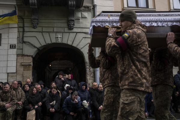 People pay their respects as soldier carry the coffin of soldier Roman Tsyhanskyi during a funeral ceremony outside the Holy Apostles Peter and Paul Church in Lviv, western Ukraine, on Friday, Feb. 24, 2023. Tsyhanskyi died near Bakhmut a week ago.(AP Photo/Petros Giannakouris)
