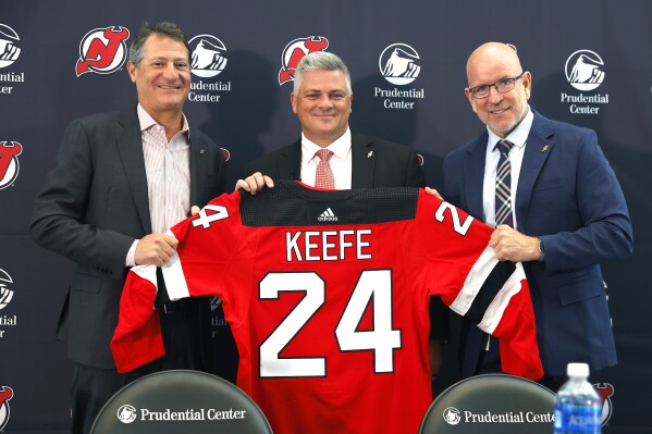 New Jersey Devils managing partner David Blitzer, left, and general manager Tom Fitzgerald, right, introduce Sheldon Keefe as the new head coach of the Devils NHL hockey team during press conference, Tuesday, May 28, 2024, in Newark, N.J. (AP Photo/Noah K. Murray)