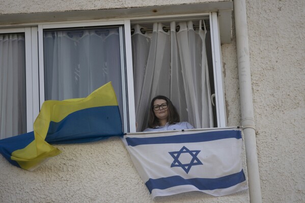 Tatyana Prima, who fled Mariupol, Ukraine, poses for a portrait with her national flag and the Israeli flag she displays outside of her apartment window in Ashkelon, southern Israel, Wednesday, Nov. 8, 2023. She thought she'd left the bombs behind when she fled after Russian troops decimated her city. Risking her life, the 38-year-old escaped with her injured husband and young daughter, bringing the family to safety in southern Israel. Yet the calm she was slowly regaining shattered on Oct. 7, when Hamas militants invaded, thrusting her onto the frontlines once again. (AP Photo/Maya Alleruzzo)
