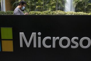 FILE - A man wearing a mask looks at this phone outside the Microsoft office in Beijing, China in a Friday, Aug. 7, 2020 file photo. Microsoft says the U.S. Labor Department is investigating its efforts to boost Black employment and leadership at the tech company. Microsoft disclosed in a blog post Tuesday, Oct. 6, 2020 that it received a letter from the agency last week asking about the company's June pledge to double the number of Black and African American people managers, senior individual contributors and senior leaders by 2025. (AP Photo/Ng Han Guan, File)
