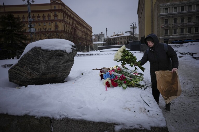 Una mujer deposita flores en honor a Alexei Navalny en el Monumento, un gran peñón de las islas Solovetsky, donde se estableció el primer campo del sistema de prisiones políticas Gulag, con el histórico edificio del Servicio Federal de Seguridad (FSB, sucesor de la KGB soviética) Al fondo, en Moscú, Rusia, el sábado 17 de febrero de 2024 por la mañana. (Foto AP/Alexander Zemlianichenko)