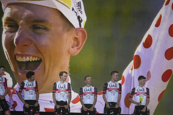 2020 and 2021 Tour de France winner Tadej Pogacar of Slovenia, right, and on screen wearing the best climber's dotted jersey, lines up with UAE Team Emirates riders during the team presentation ahead of the Tour de France cycling race in Copenhagen, Denmark, Wednesday, June 29, 2022. The race starts Friday, July 1, the first stage is an individual time trial over 13.2 kilometers (8.2 miles) with start and finish in Copenhagen. (AP Photo/Daniel Cole)