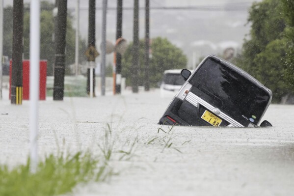 A vehicle is stuck on a street flooded due to a heavy rain in Kurume, Fukuoka prefecture, southern Japan Monday, July 10, 2023. Torrential rain is pounding southwestern Japan, triggering floods and mudslides Monday as weather officials issued emergency heavy rain warning in parts of on the southern most main island of Kyushu. (Kyodo News via AP)
