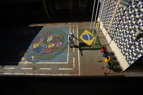 A public health worker fumigates a public school playground as part of a campaign against dengue-promoting mosquitoes, in the Sao Sebastiao neighborhood of Brasilia, Brazil, March 9, 2024. (AP Photo/Eraldo Peres)