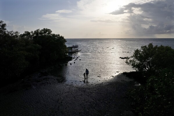 A mother and her child walk along a shoreline at the coastal village of Calatagan, Batangas province, Philippines on Wednesday, Aug. 9, 2023. The Philippines is seeing one of the world's biggest buildouts of natural gas infrastructure. But the buildout raises serious questions about the health of nearby coral reefs and fishing communities. (AP Photo/Aaron Favila)