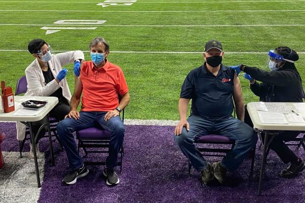 FILE - Democratic Minnesota Gov. Tim Walz, second from right, and former Republican Gov. Tim Pawlenty, second from left, receive doses of the single-shot Johnson & Johnson vaccine at a vaccination site at a Minnesota Vikings NFL football team practice facility on March 30, 2021, in Eagan, Minn. Fewer than 20% of Minnesotans are current on their COVID-19 shots ahead of the Christmas holiday, and health officials said Tuesday, Dec. 13, 2022, that has them worried. (AP Photo/Mohamed Ibrahim, File)
