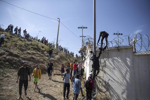 FILE - In this May 18, 2021, file photo, people climb a fence in the area at the Spain-Morocco border, outside the Spanish enclave of Ceuta. Thousands of would-be migrants converged on the Moroccan border town of Fnideq this week, part of an extraordinary mass effort to swim or scale barbed-wire fences to get into Spain for a chance at a new life. (AP Photo/Mosa'ab Elshamy)