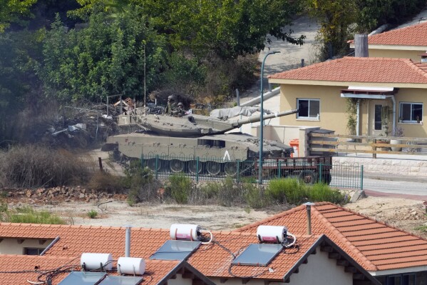 FILE - An Israeli tank is deployed between houses in the Israeli town of Metula as seen from the Lebanese side of the Lebanese-Israeli border in the southern village of Kfar Kila, Lebanon, Monday, Oct. 9, 2023. (AP Photo/Hassan Ammar, File)