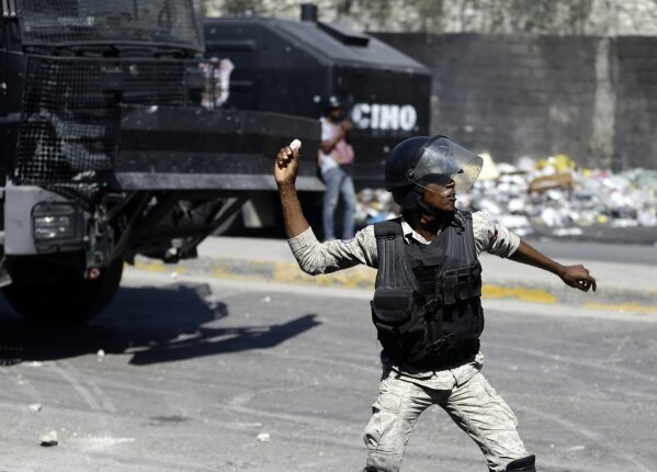 A police officer throws a stone at protesters during a protest to demand the resignation of Haiti's president Jovenel Moise in Port-au-Prince, Haiti, Wednesday, Jan. 20, 2021. Moise has one more year in power, but a growing groundswell of opposition is organizing protests and demanding he resign next month amid spiraling crime and a crumbling economy. ( AP Photo/ Dieu Nalio Chery)