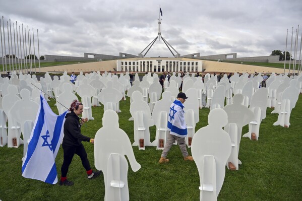 Supporters of Israel walk past cutout cardboard effigies, representing Israeli hostages, during a protest outside Parliament House in Canberra, Australia, Tuesday, Nov. 28, 2023. Relatives and a friend of Israelis kidnapped and killed by Hamas visited Australia's Parliament House on Tuesday, sharing personal stories to lobby for international support for all hostages to be freed and to support Israel's war effort.(Mick Tsikas/AAP Image via AP)