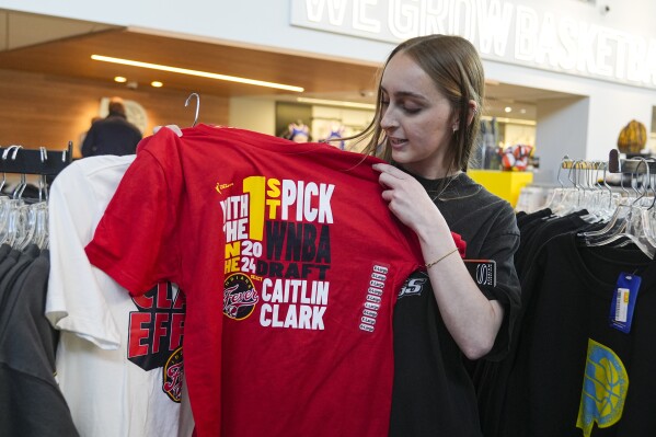 Shelby Tekulve, 20, displays one of the Caitlin Clark shirts she was purchasing in the Indiana Fever team store in Indianapolis, Tuesday, April 16, 2024. The Fever selected Clark as the No. 1 overall pick in the WNBA basketball draft. (AP Photo/Michael Conroy)