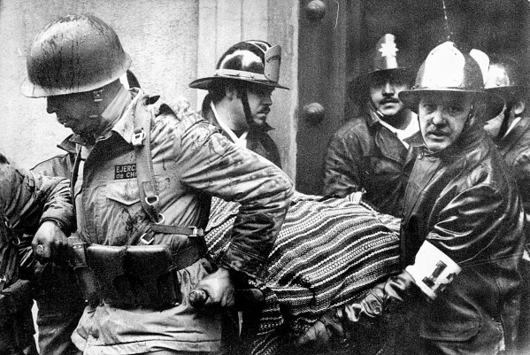 FILE - Soldiers and firefighters carry the body of Chilean President Salvador Allende, wrapped in a Bolivian poncho, out of La Moneda presidential palace after it was bombed during a coup by Gen. Augusto Pinochet in Santiago, Chile, Sept. 11, 1973. (AP Photo/El Mercurio, File)