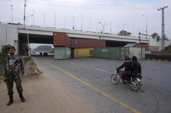 A paramilitary soldier stands guard as a motorcyclist drives on a highway, which partially closed with shipping containers ahead of a planned rally by supporters of imprisoned former Prime Minister Imran Khan's Pakistan Tehreek-e-Insaf party, in Islamabad, Pakistan, Saturday, Nov. 23, 2024. (AP Photo/Anjum Naveed)