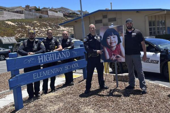 FILE - In this image provided by the Seaside Police Department, interim Police Chief Nick Borges, second from right, and Det. Joshua Parker, right, stand next to a photo of Anne Pham outside Highland Elementary School in Seaside, Calif., on July 7, 2022. Robert Lanoue, who was arrested in Reno, Nev., was extradited Friday, July 22, 2022, to California, where he entered a not guilty plea in the 1982 killing of a 5-year-old Anne Pham. The child disappeared while walking to her kindergarten class in Seaside, Calif. Her body was found two days later in the former Fort Ord. (Seaside Police Department via AP, File)