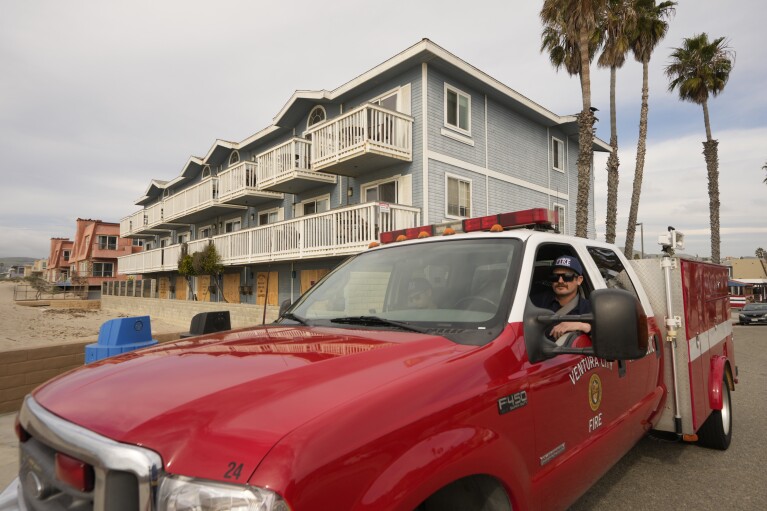 Ventura County Paramedics stand outside the boarded-up Inn on the Beach Hotel in Ventura, Calif., Wednesday, Jan. 31, 2024. The Inn is temporarily closed due to flood damage as a wave hit the first-floor level of the hotel, breaking the exterior windows. (AP Photo/Damian Dovarganes)