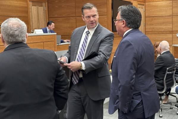 In this photo from Friday, Nov. 3, 2023, Kansas Attorney General Kris Kobach, center, confers with state Solicitor General Tony Powell, right, as a legal team that also includes attorney Brad Schlozman, left, prepares for a Kansas Supreme Court hearing on a legal challenge to state election laws, in Topeka, Kan. The Supreme Court has revived a lawsuit from four voting rights groups against a law making it a felony to impersonate elections officials. (AP Photo/John Hanna)