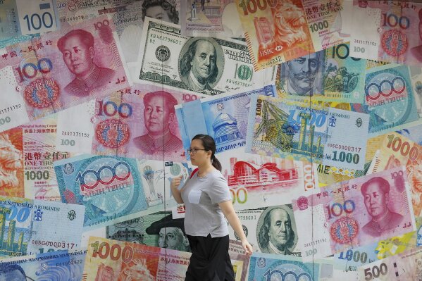 FILE _ In this Aug. 6, 2019, file photo, a woman walks by a money exchange shop decorated with different countries currency banknotes at Central, a business district in Hong Kong. China has announced it will raise tariffs on $75 billion of U.S. products in retaliation for President Donald Trump's planned Sept. 1 duty increase in a war over trade and technology policy. (AP Photo/Kin Cheung, File)