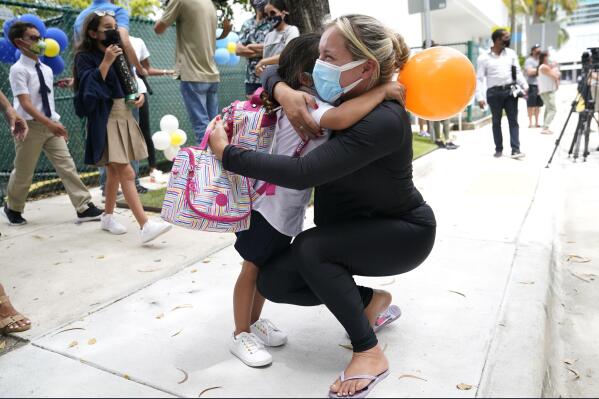 FILE- In this Monday, Aug. 23, 2021, file photo,  Carol Basilio, right, hugs her daughter Giovanna outside of iPrep Academy on the first day of school, in Miami. A judge has ruled that Florida school districts may impose mask mandates. Leon County Circuit Judge John C. Cooper on Friday agreed with a group of parents who claimed in a lawsuit that Gov. Ron DeSantis' ban on the mandates is unconstitutional and cannot be enforced. (AP Photo/Lynne Sladky, File)