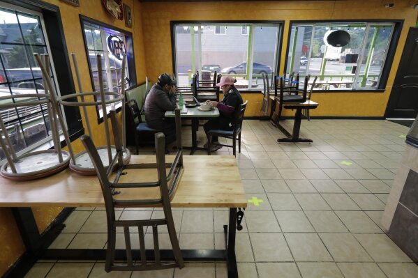 In this April 27, 2020 photo, Antonia Lopez, right, sits with her son, Isaac, 19, in the dining room of their Tacos El Tajin restaurant in Algona, Wash., on the first day it was open for take-out orders after the death of her husband, Tomas Lopez, 44, who died of COVID-19 on April 2. Lopez was a beloved fixture wherever he sold tacos from his family's bright green taco truck, and now his family members are hoping to continue the business with the same spirit of friendship and joy for his customers that their father and husband had. (AP Photo/Ted S. Warren)